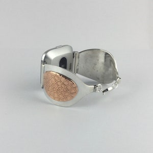 May include: A silver watch band with a rose gold patterned accent. The band is designed to fit a square-shaped watch.