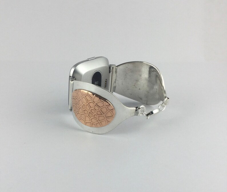 May include: A silver watch band with a rose gold patterned accent. The band is designed to fit a square-shaped watch.