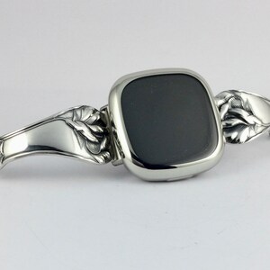 Peut inclure: Un bracelet de montre argent&eacute; avec un motif floral. Le cadran de la montre est noir et de forme carr&eacute;e.