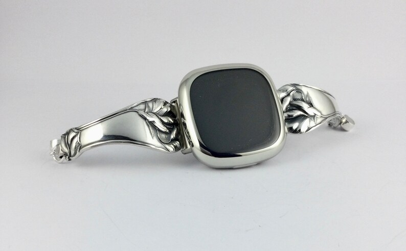 Peut inclure: Un bracelet de montre argent&eacute; avec un motif floral. Le cadran de la montre est noir et de forme carr&eacute;e.