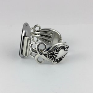 May include: Silver bracelet made from a vintage silverware fork. The bracelet is designed to fit a watch or smart watch. The bracelet has a decorative design with a floral pattern.