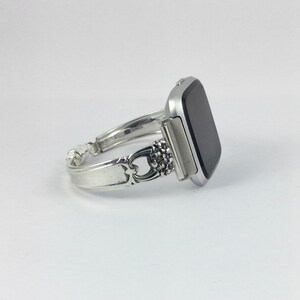 May include: A silver watch band made from a repurposed silverware piece. The band is attached to a silver smartwatch with a black screen.
