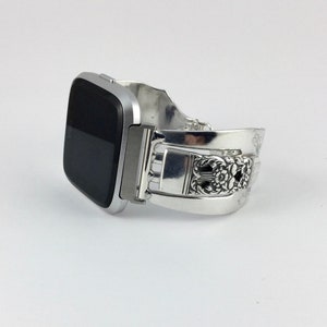 May include: A silver smartwatch with a black screen on a silver spoon bracelet.