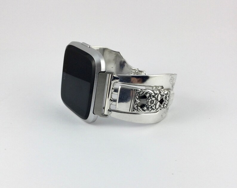 May include: A silver smartwatch with a black screen on a silver spoon bracelet.