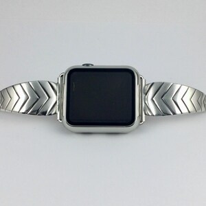 May include: A silver watch band with a chevron pattern. The band is designed to fit a smartwatch.