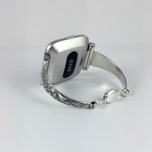May include: A silver smartwatch with a floral patterned band. The watch is on a white background.