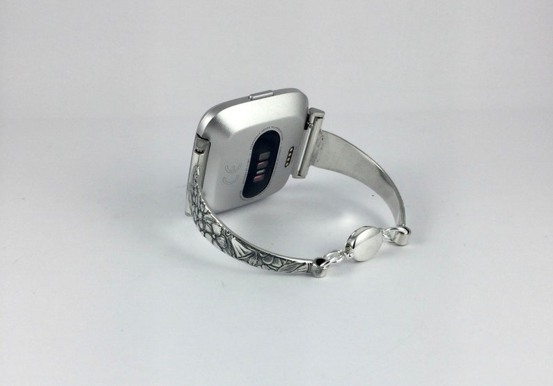 May include: A silver smartwatch with a floral patterned band. The watch is on a white background.