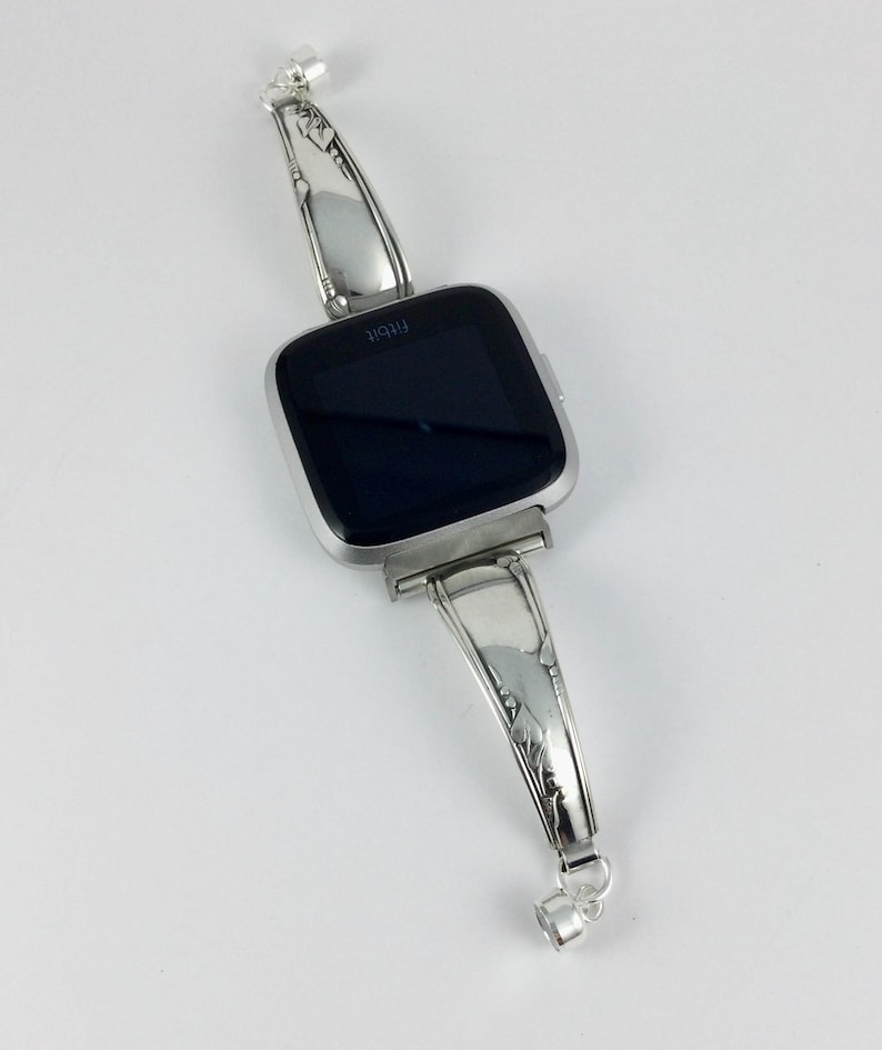 Peut inclure: Un bracelet de montre argent&eacute; fabriqu&eacute; &agrave; partir d'une pi&egrave;ce de couverts r&eacute;utilis&eacute;e. Le bracelet est con&ccedil;u pour s'adapter &agrave; une montre connect&eacute;e de forme carr&eacute;e. Le bracelet pr&eacute;sente un design orn&eacute; avec un motif floral.