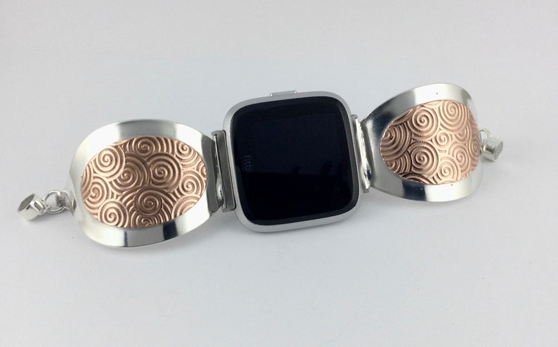 May include: A silver and rose gold watch band with a swirling pattern. The band is designed to fit a square-shaped smartwatch.