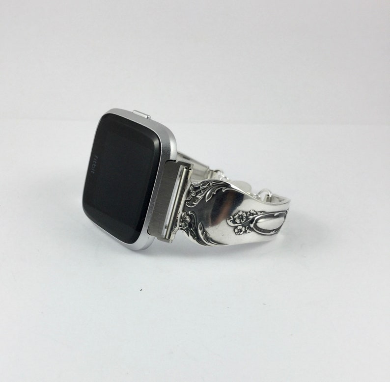 May include: Silver-toned Fitbit smartwatch with a unique, ornate, silver-toned band made from a repurposed spoon.