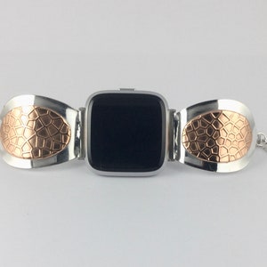 May include: A silver and rose gold watch band with a geometric pattern. The band is designed to fit a square-shaped smartwatch.