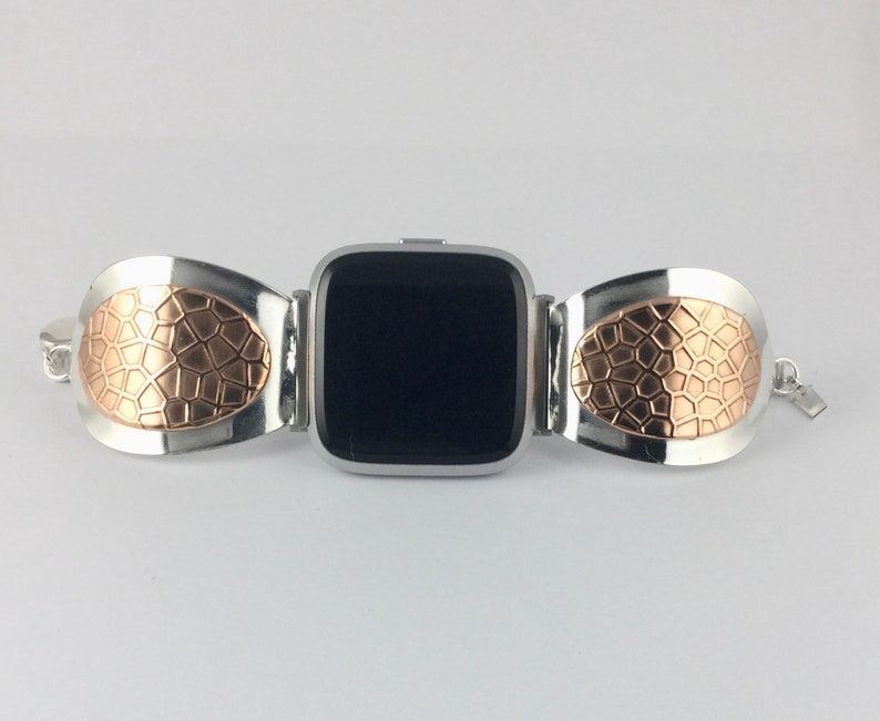 May include: A silver and rose gold watch band with a geometric pattern. The band is designed to fit a square-shaped smartwatch.