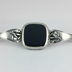 Peut inclure: Un bracelet de montre argent&eacute; avec un motif floral. Le cadran de la montre est noir et de forme carr&eacute;e.
