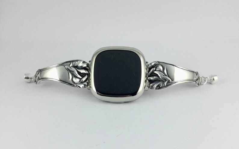 Peut inclure: Un bracelet de montre argent&eacute; avec un motif floral. Le cadran de la montre est noir et de forme carr&eacute;e.