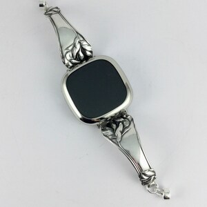 Peut inclure: Un bracelet en argent avec une pierre noire carr&eacute;e au centre. Le bracelet est orn&eacute; d'un motif floral aux extr&eacute;mit&eacute;s.