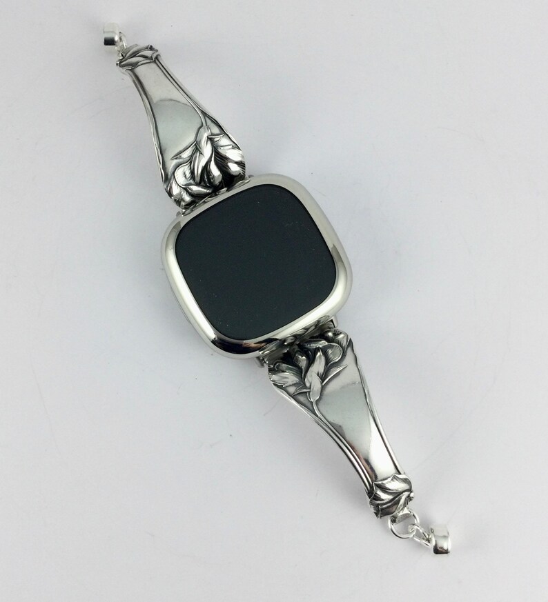 Peut inclure: Un bracelet en argent avec une pierre noire carr&eacute;e au centre. Le bracelet est orn&eacute; d'un motif floral aux extr&eacute;mit&eacute;s.