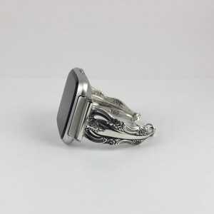 May include: A silver smartwatch with a silver, ornate, decorative band made from silverware.