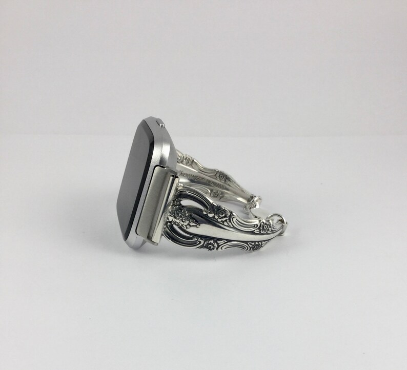 May include: A silver smartwatch with a silver, ornate, decorative band made from silverware.