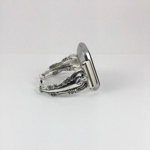May include: A silver watch band made from a repurposed silverware piece. The band is decorated with floral designs and has a silver watch face.