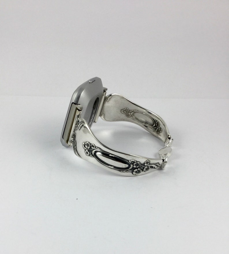 May include: A silver watch with a square face and a unique, ornate, silver spoon-shaped band.