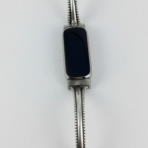 May include: A silver bracelet with a black rectangular watch face. The bracelet has a beaded design and a small silver charm at the end.