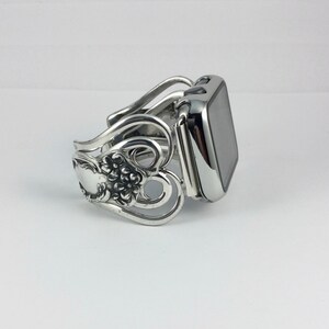 May include: Silver-toned watch band with a decorative floral and scroll design. The band is made from repurposed silverware, featuring spoon and fork elements. The watch face is a shiny, reflective black.