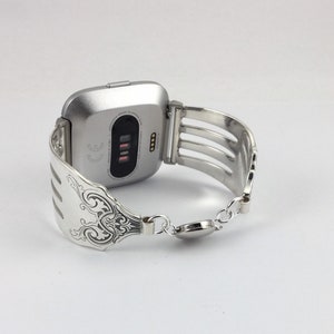 Pu&ograve; includere: Smartwatch argentato con un cinturino a forma di forchetta argentata. Il quadrante dell'orologio &egrave; nero e ha un piccolo display con testo bianco. Il cinturino &egrave; fatto di una forchetta con un design decorativo.