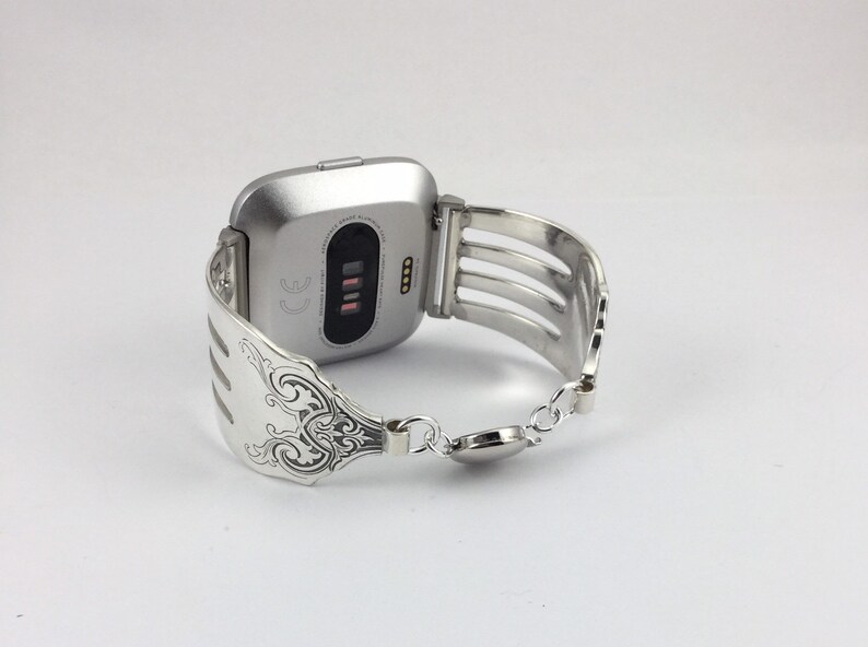 Pu&ograve; includere: Smartwatch argentato con un cinturino a forma di forchetta argentata. Il quadrante dell'orologio &egrave; nero e ha un piccolo display con testo bianco. Il cinturino &egrave; fatto di una forchetta con un design decorativo.