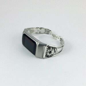 May include: Silver-toned smartwatch with a black screen, integrated into a bracelet crafted from ornate silverware. The bracelet features floral and beaded details, creating a unique and decorative accessory.