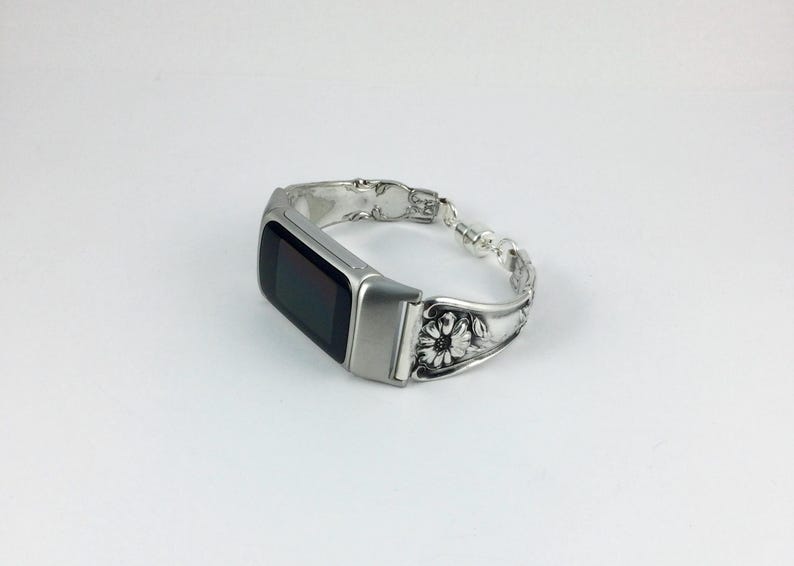 May include: Silver-toned smartwatch with a black screen, integrated into a bracelet crafted from ornate silverware. The bracelet features floral and beaded details, creating a unique and decorative accessory.