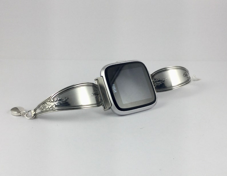 May include: A silver Fitbit smartwatch attached to a silver bracelet made from a repurposed spoon.