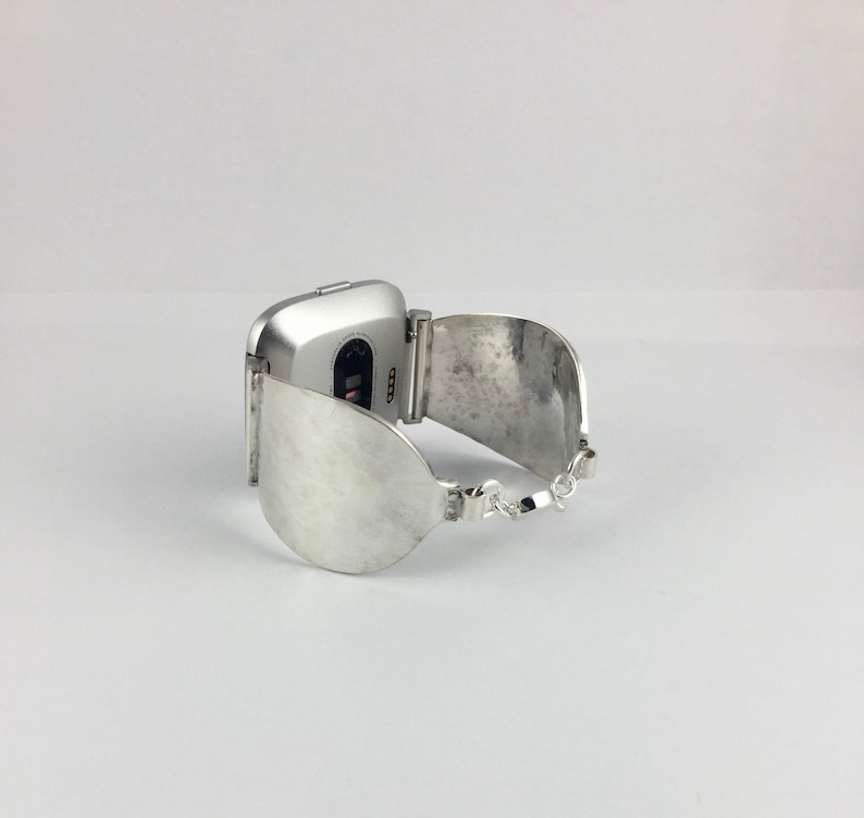 May include: Silver watch band with a curved, silver cuff design. The watch face is square and silver.
