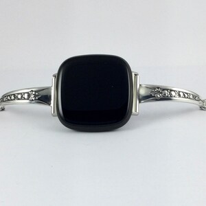 Puede incluir: Una pulsera de plata con una piedra negra cuadrada en el centro. La pulsera tiene una cadena delicada y dise&ntilde;os florales en los lados.