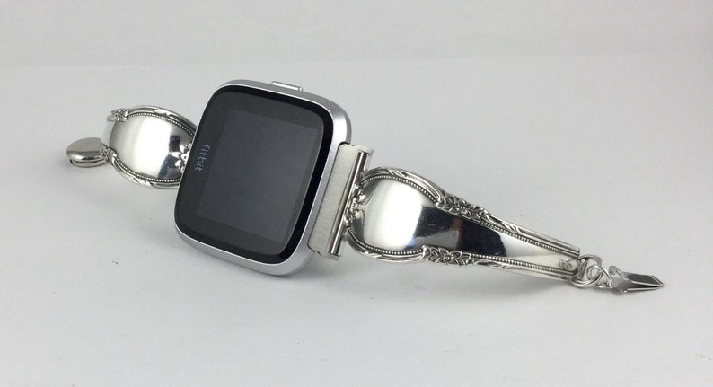 May include: A silver Fitbit smartwatch with a custom-made band crafted from a vintage silverware spoon.
