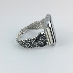 May include: A silver-toned watch band crafted from ornate silverware. The band features a floral design and connects to a silver watch face. The watch band is a unique accessory, combining functionality with vintage style.