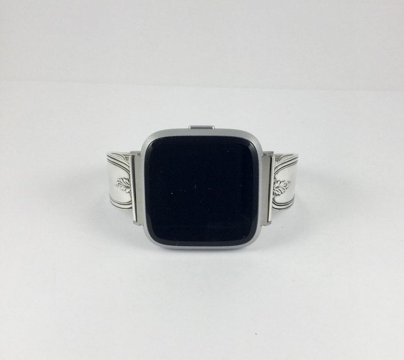 May include: A silver watch band made from a repurposed silverware piece. The band is designed to fit a square-shaped smartwatch.