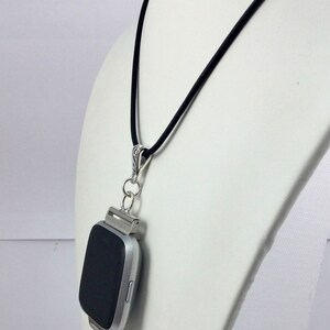 May include: A silver smartwatch pendant necklace with a black screen, suspended from a black cord. The pendant features a cluster of blue crystal beads. The necklace is displayed on a white mannequin.