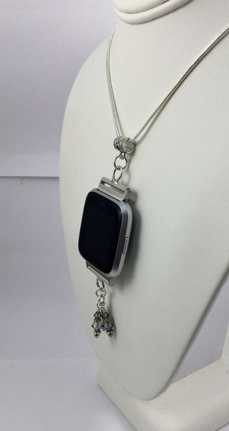 K&ouml;nnte beinhalten: Eine silberne Halskette mit einem silbernen Uhrenzifferblatt-Anh&auml;nger und einer silbernen Kette. Das Zifferblatt der Uhr ist schwarz und die Halskette hat einen silbernen Anh&auml;nger mit schillernden Kristallen.