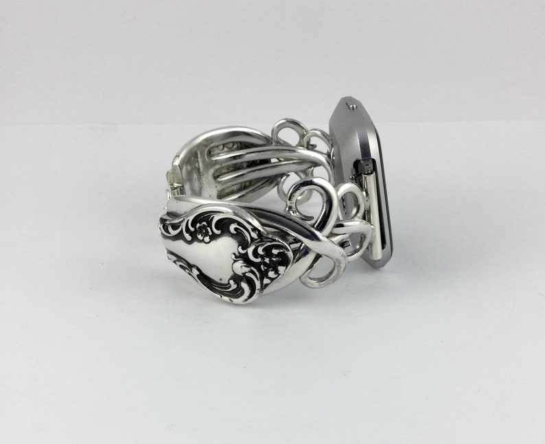 May include: Silver watch band made from a vintage silverware fork. The band is designed to fit a square-shaped smartwatch.