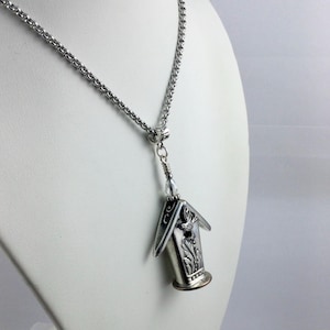 May include: Silver-toned birdhouse pendant necklace. The pendant features intricate floral and bird details. The necklace has a delicate chain and is displayed on a white bust. The birdhouse pendant is approximately 1 inch in height.