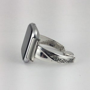 May include: A silver smartwatch with a black face is attached to a silver bracelet with an ornate design.