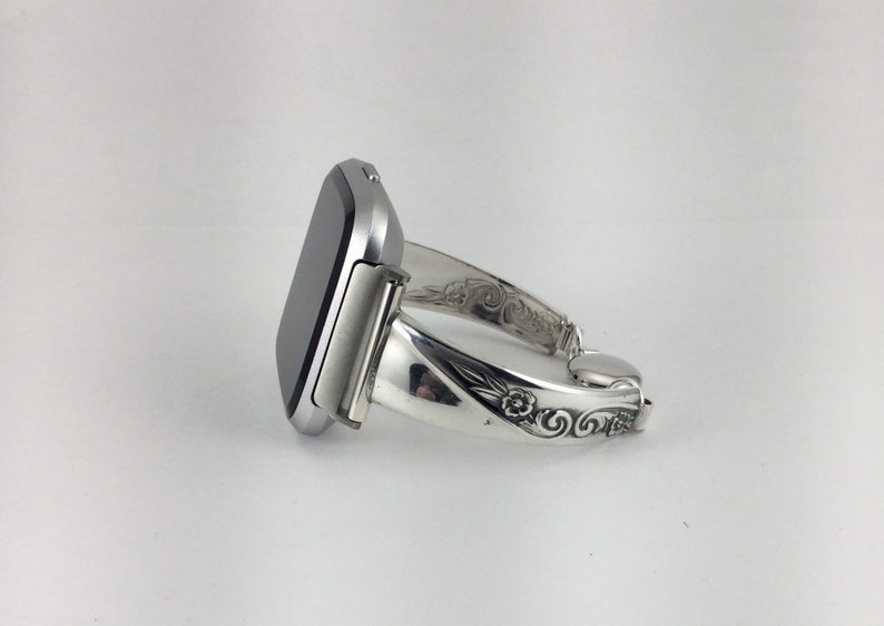 May include: A silver smartwatch with a black face is attached to a silver bracelet with an ornate design.