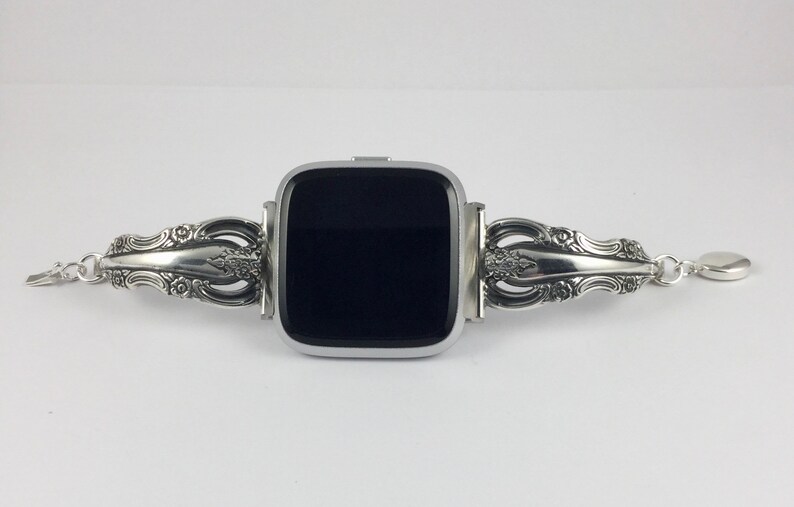 May include: A silver smartwatch with a black screen, attached to a silver watch band made from a repurposed silverware handle.