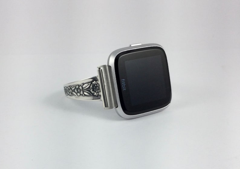 Puede incluir: Smartwatch Fitbit plateado con una banda floral decorativa.