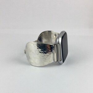 May include: A silver watch band with a hammered texture. The band is designed to fit a square-shaped smartwatch.