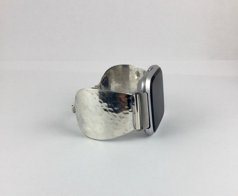 May include: A silver watch band with a hammered texture. The band is designed to fit a square-shaped smartwatch.