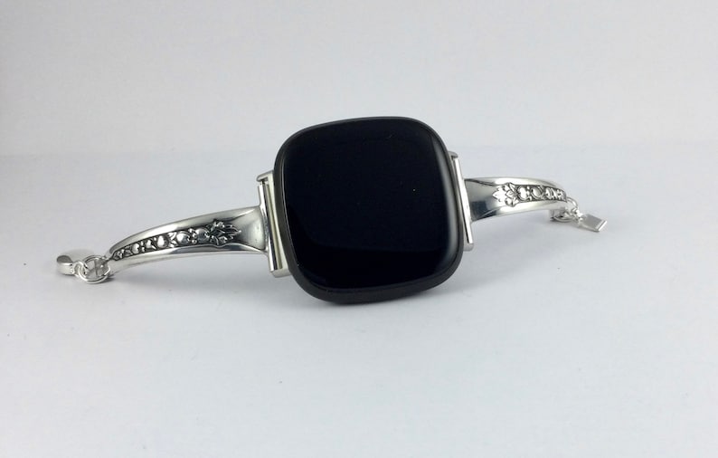 Puede incluir: Una pulsera de plata con una piedra de vidrio negra cuadrada en el centro. La pulsera tiene un dise&ntilde;o floral en la banda.
