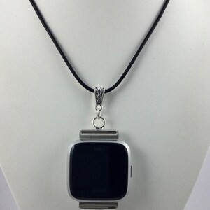 May include: A silver Fitbit watch pendant necklace with a black watch face and a cluster of blue beads. The pendant hangs from a black cord necklace.