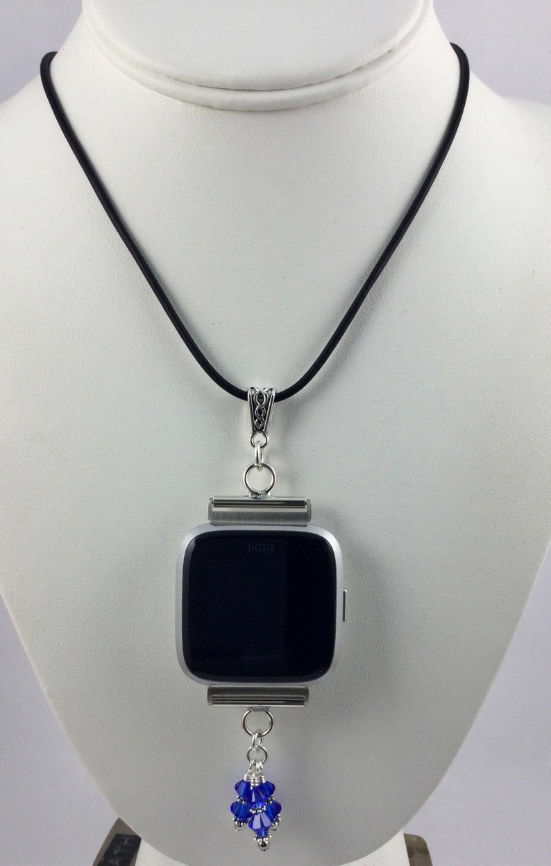 May include: A silver Fitbit watch pendant necklace with a black watch face and a cluster of blue beads. The pendant hangs from a black cord necklace.