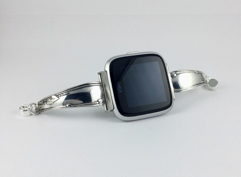 Peut inclure: Une montre connect&eacute;e Fitbit argent&eacute;e fix&eacute;e &agrave; un bracelet argent&eacute; fabriqu&eacute; &agrave; partir d'une pi&egrave;ce de couverts r&eacute;utilis&eacute;e.